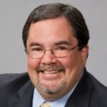 chris-connolly-headshot - The Cruise Headquarters the cruise headquarters professional headshot of a smiling man wearing a dark suit light blue shirt and glasses