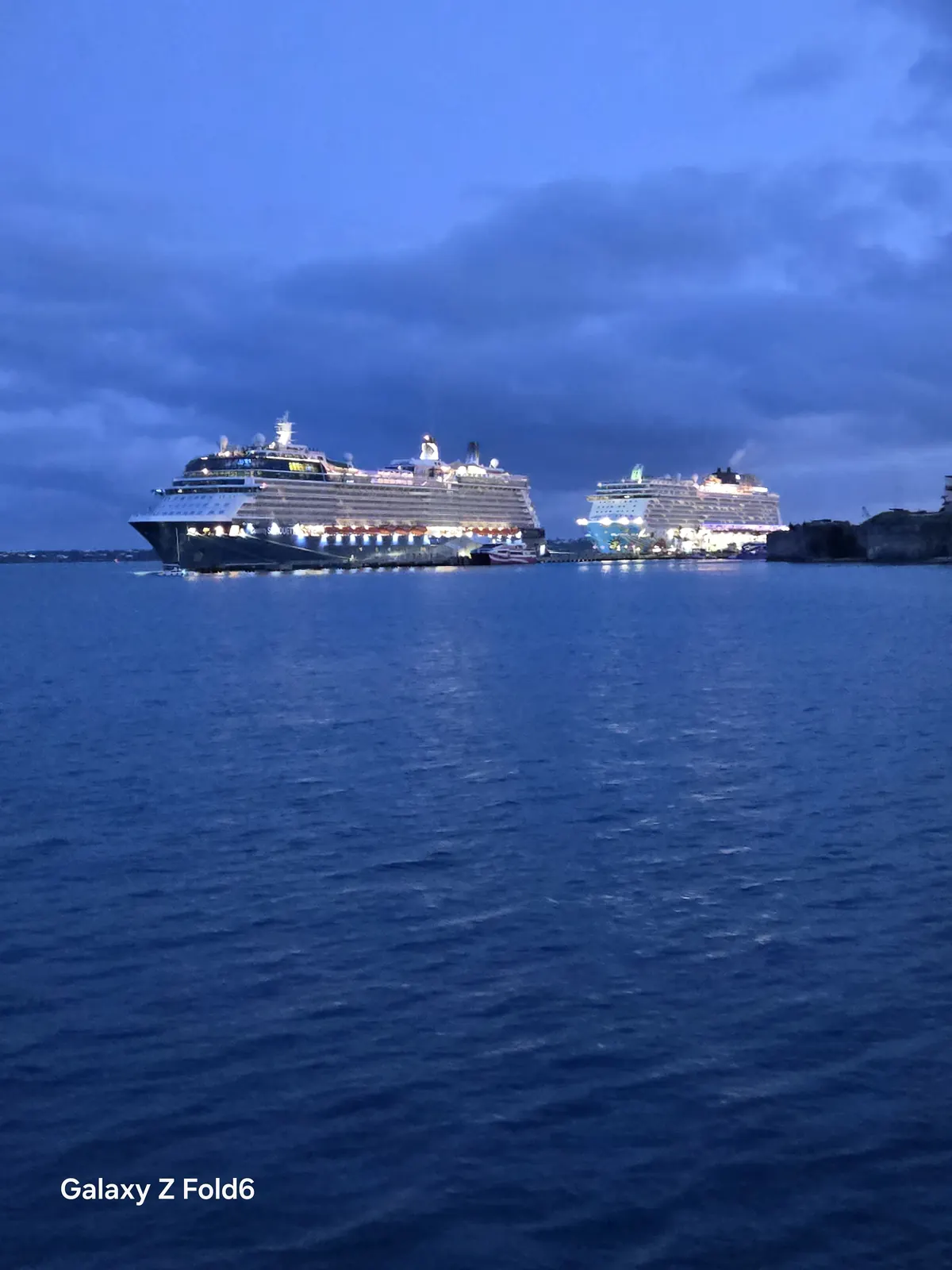 the cruise hq two cruise ships with lights on docked at royal naval dockyard bermuda in the evening