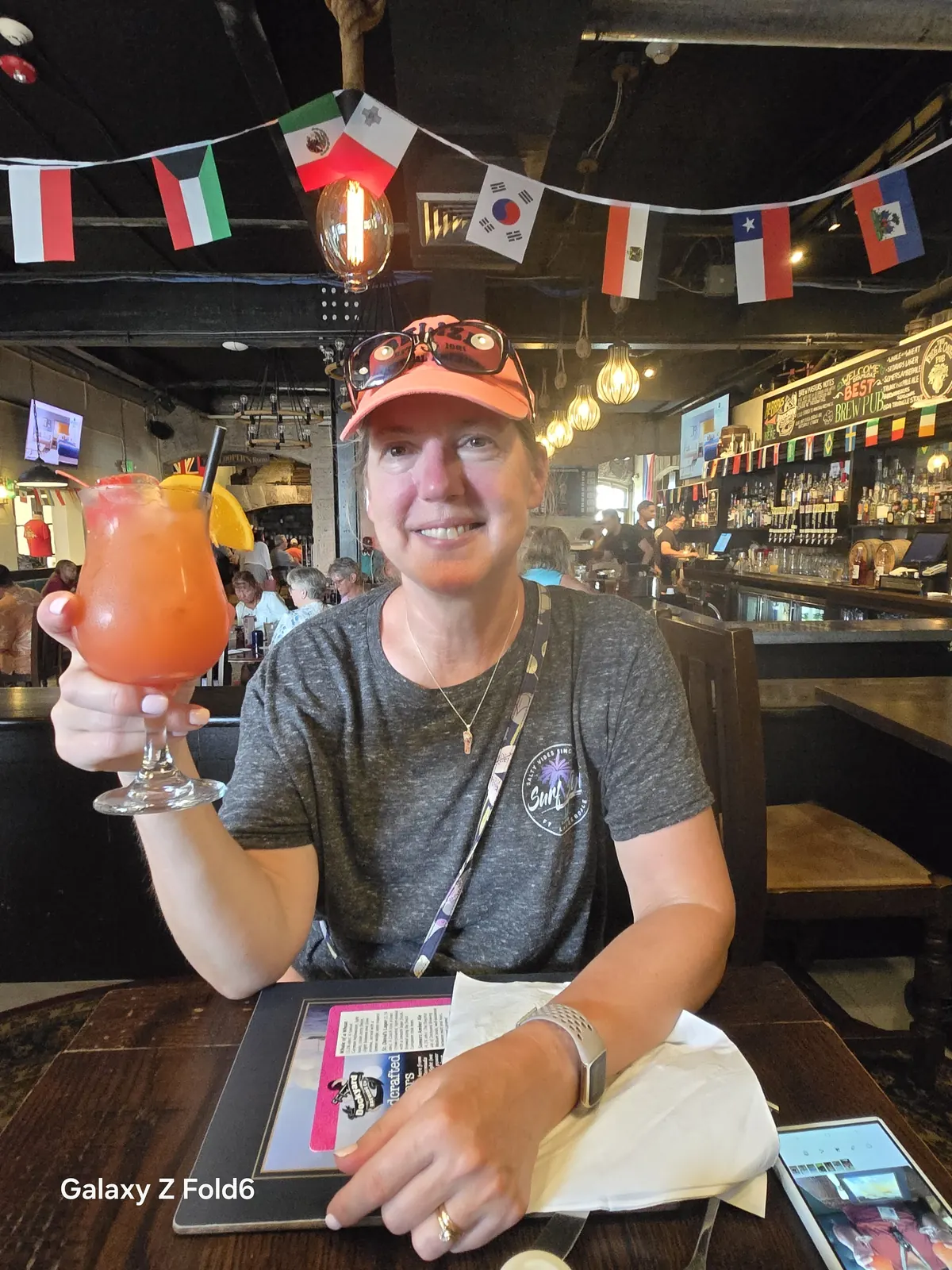 the cruise hq smiling cruiser raising a rum swizzle cocktail in a flag decorated pub at royal naval dockyard