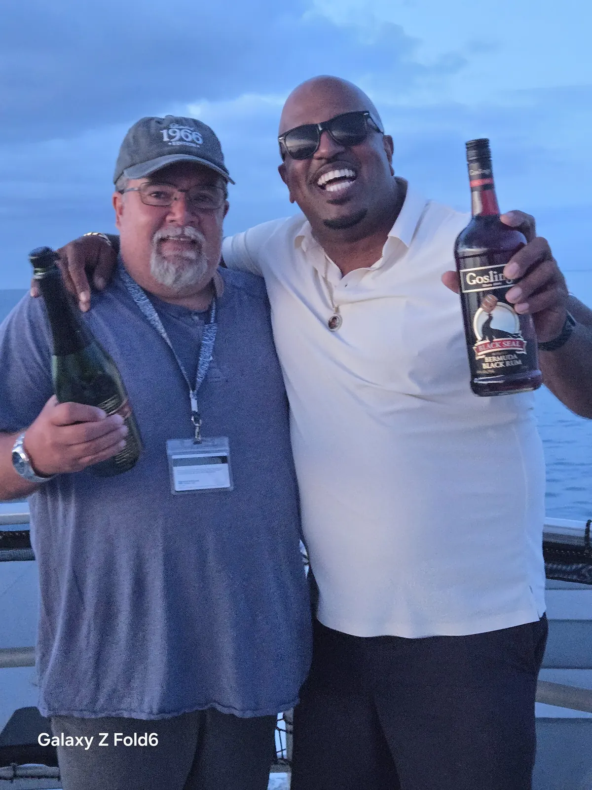 the cruise hq guest and host laughing with bottles of sparkling wine and gosling's rum at dusk in bermuda