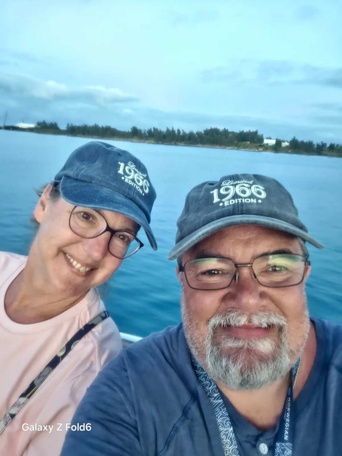 the cruise hq couple in matching 1966 caps smiling on a boat in bermuda's great sound with the shoreline behind