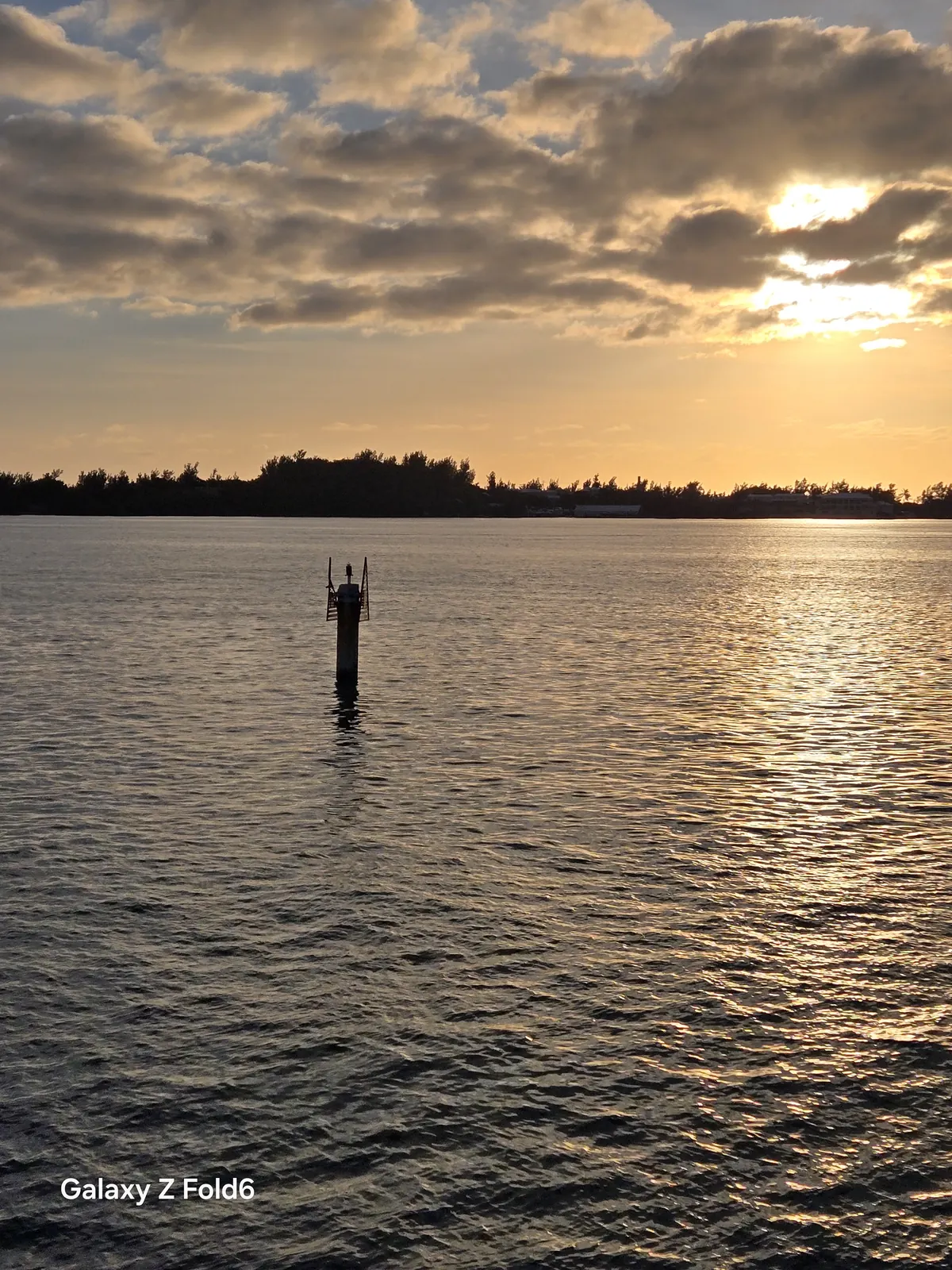 the cruise hq sun setting behind clouds over bermuda's great sound with a navigation marker in the water