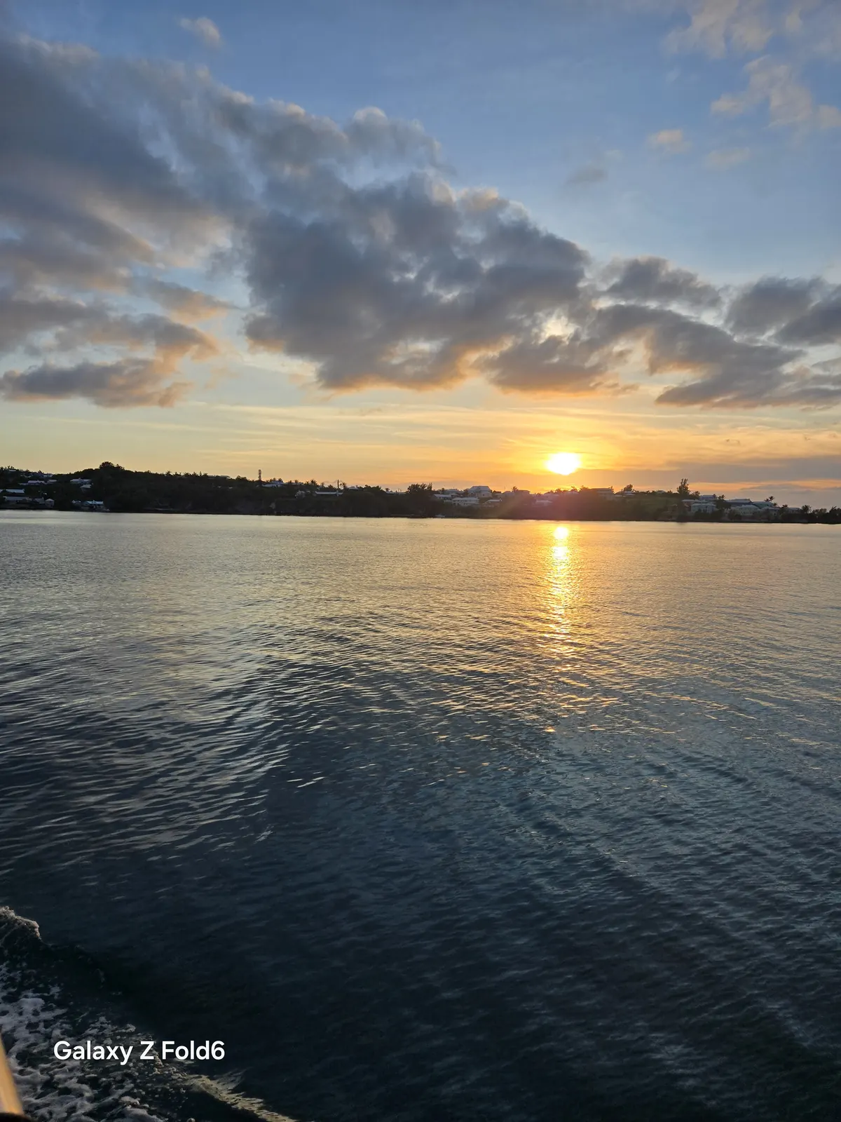 the cruise hq sun setting over a tree lined bermuda shore with clouds above the great sound