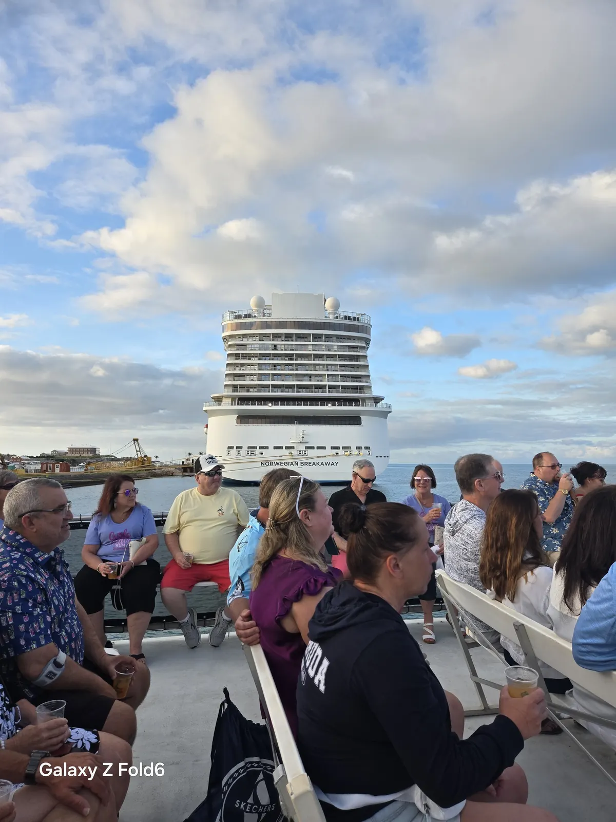 the cruise hq cruise passengers seated on the open deck of a tour boat with norwegian breakaway docked behind at king's wharf bermuda