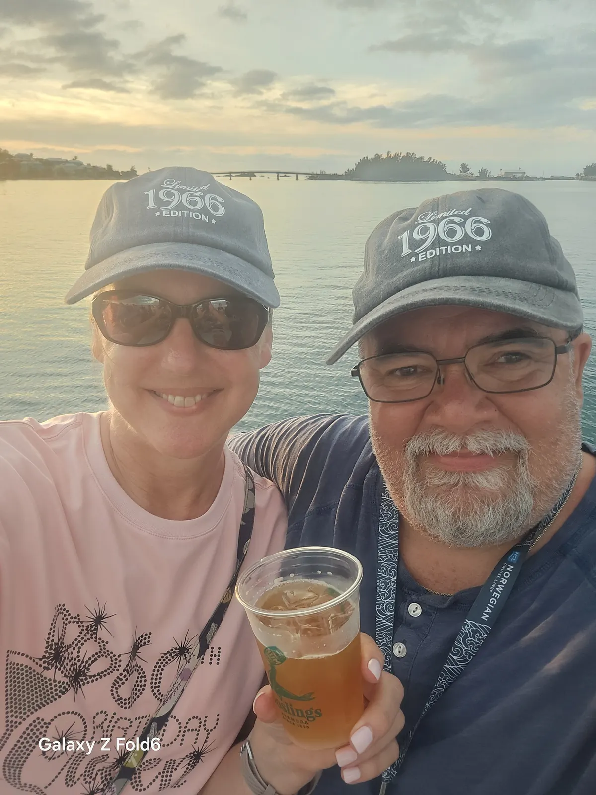 the cruise hq two smiling cruisers in matching caps take a selfie with a rum swizzle on the great sound bermuda