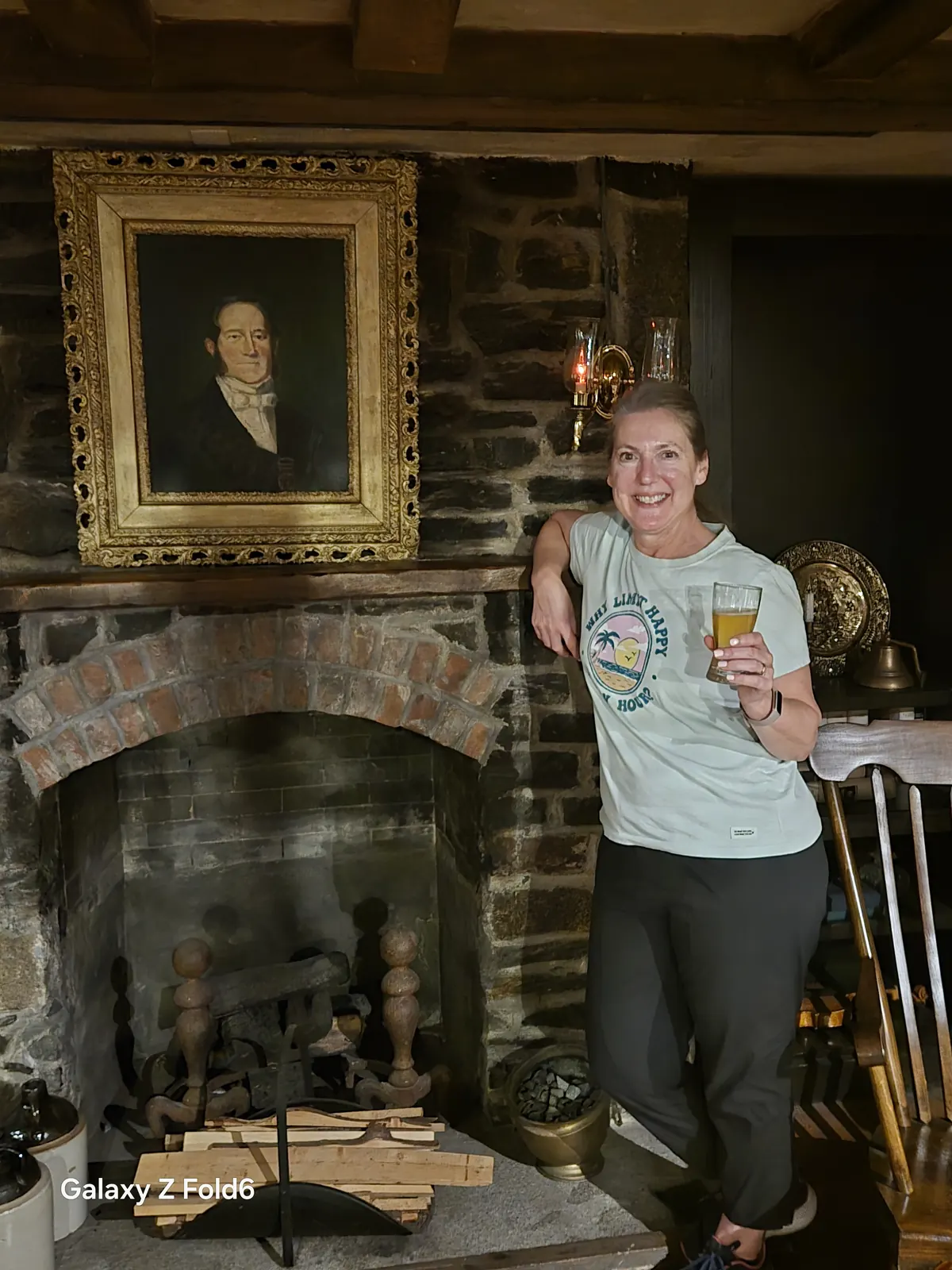 the cruise hq smiling visitor holding a beer beside a stone fireplace and framed portrait at alexander keith's Brewery in Halifax