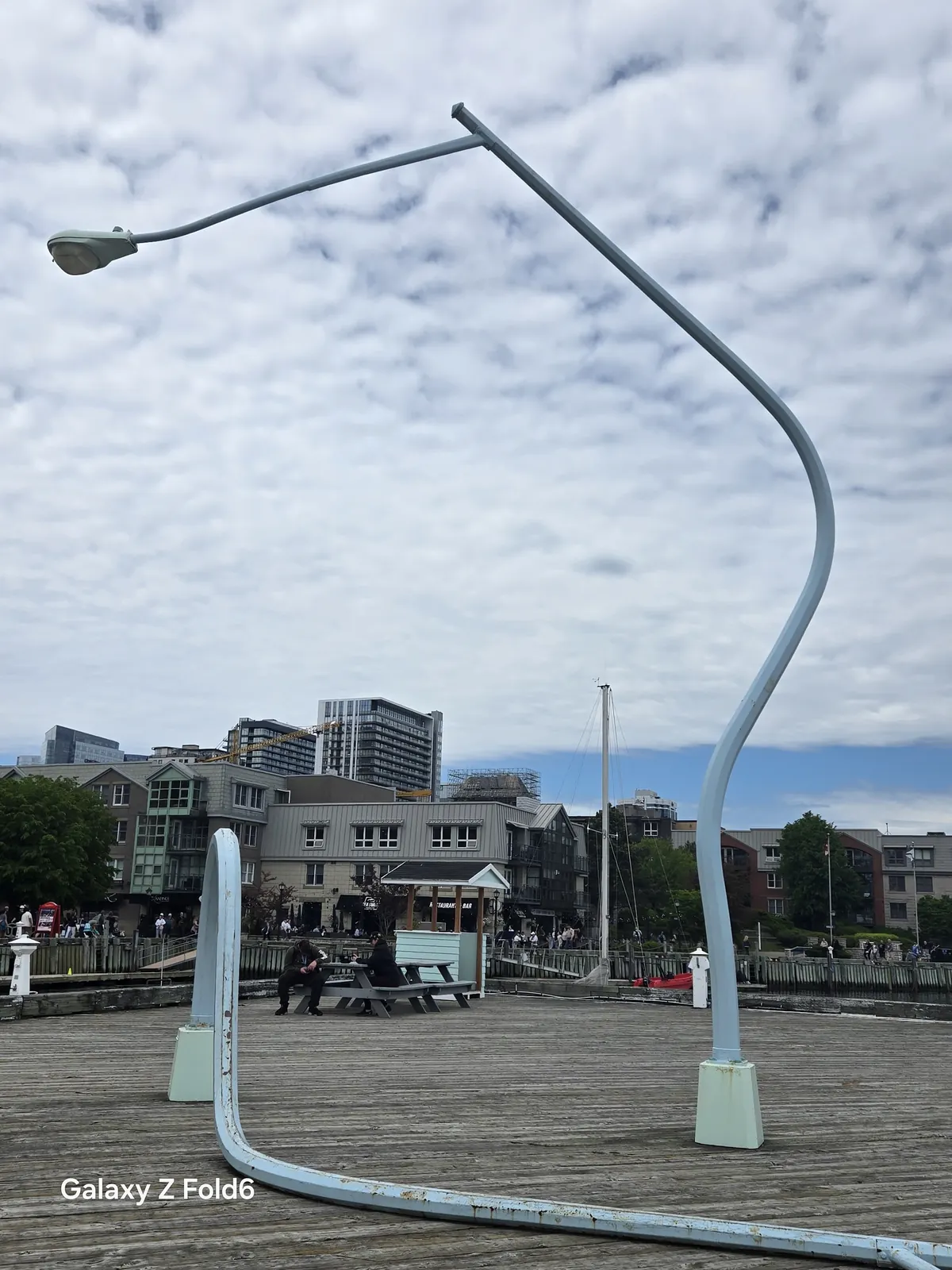 the cruise hq bent lamppost sculpture arching over the wooden boardwalk with waterfront buildings behind on the halifax waterfront