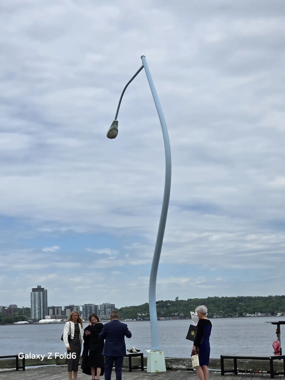 the cruise hq tall curved lamppost on the boardwalk with halifax harbour and the dartmouth skyline behind on the halifax waterfront