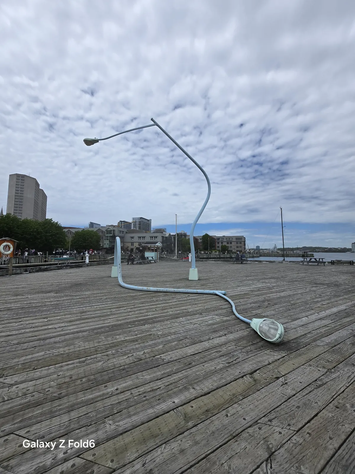 the cruise hq lamppost sculpture slumped across the wooden wharf with its light resting on the deck on the halifax waterfront