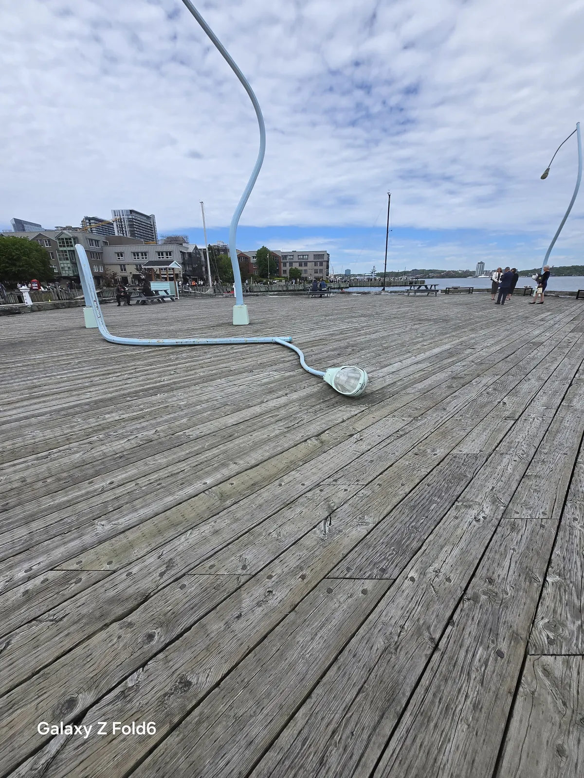 the cruise hq wide view of the wharf deck with a fallen lamppost sculpture and a second bent lamppost by the harbour on the halifax waterfront
