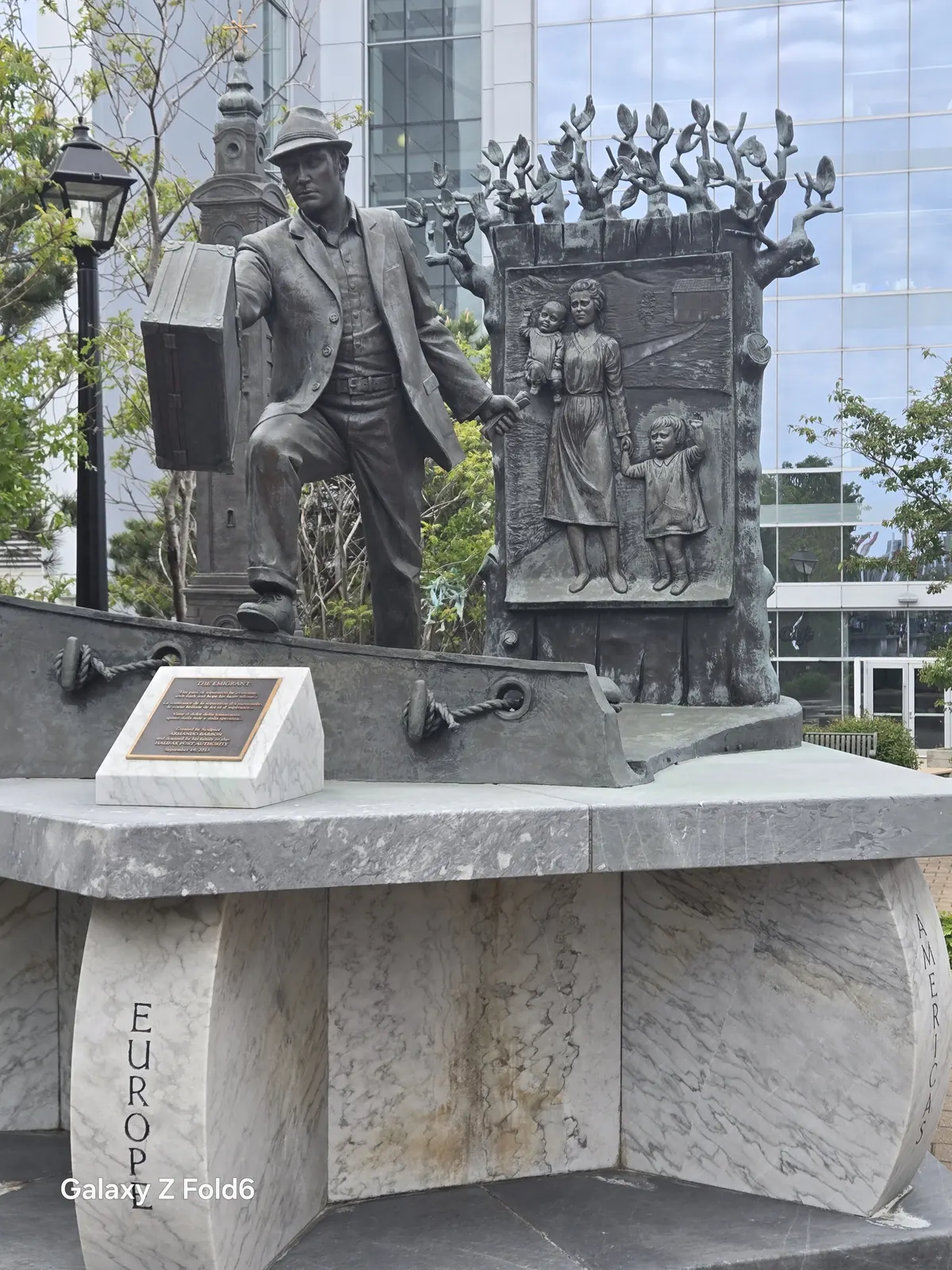 the cruise hq bronze statue of a man with a suitcase stepping off a ship on a marble base carved europe and america on the halifax waterfront