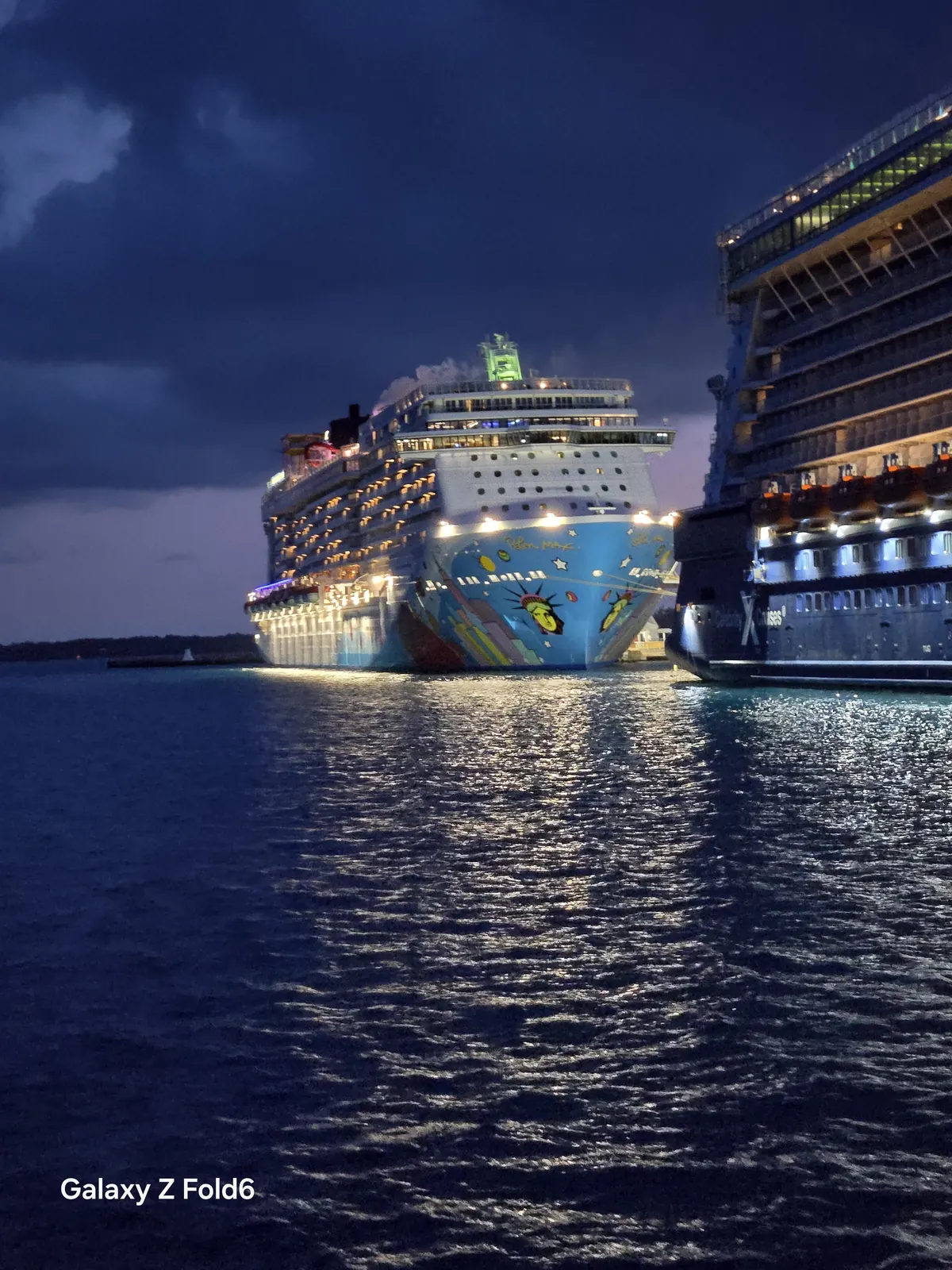 the cruise hq norwegian breakaway with its colourful hull art docked beside another ship at night in bermuda