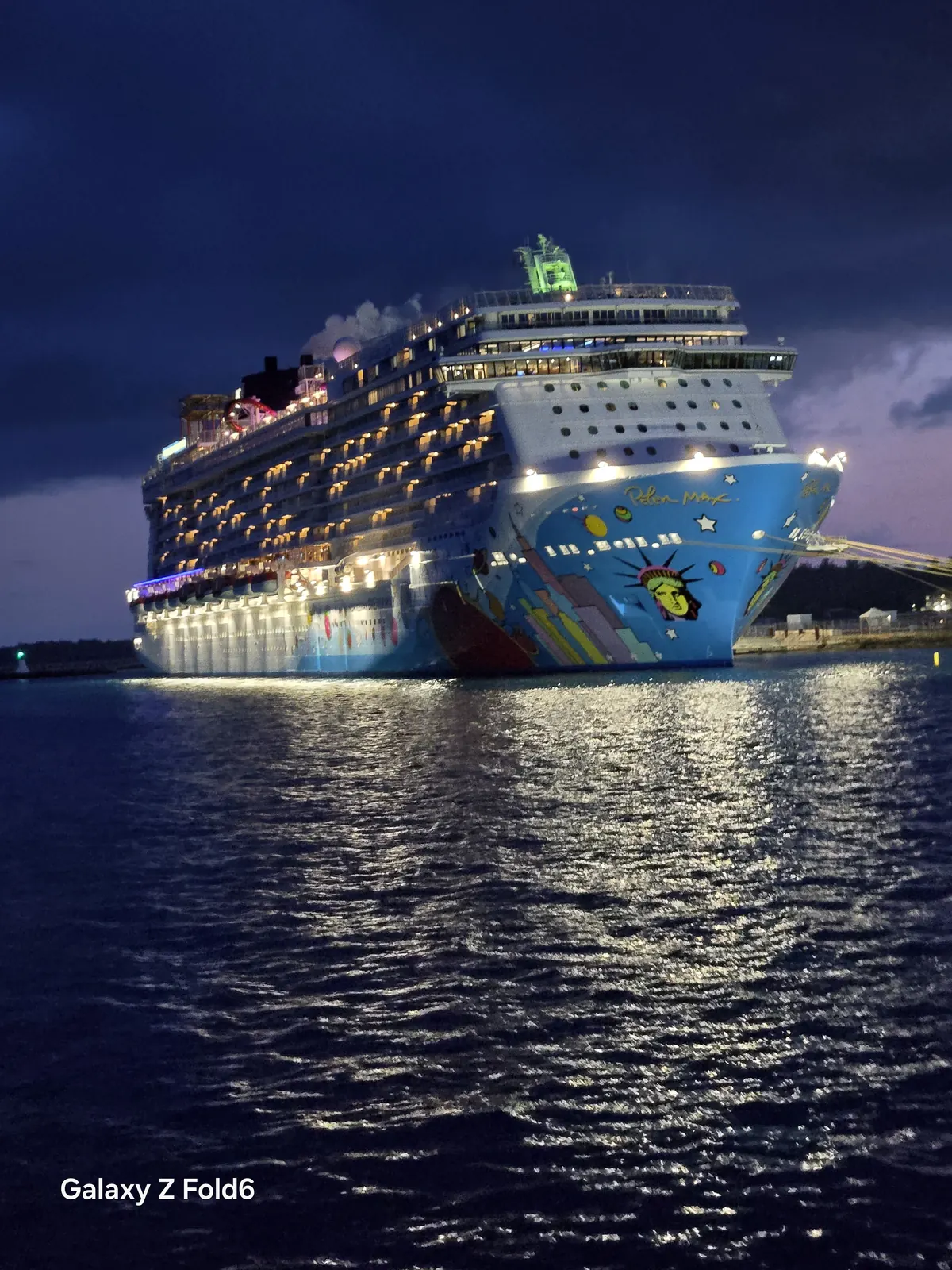 the cruise hq bow of norwegian breakaway showing peter max hull art and lights reflecting on the water in bermuda