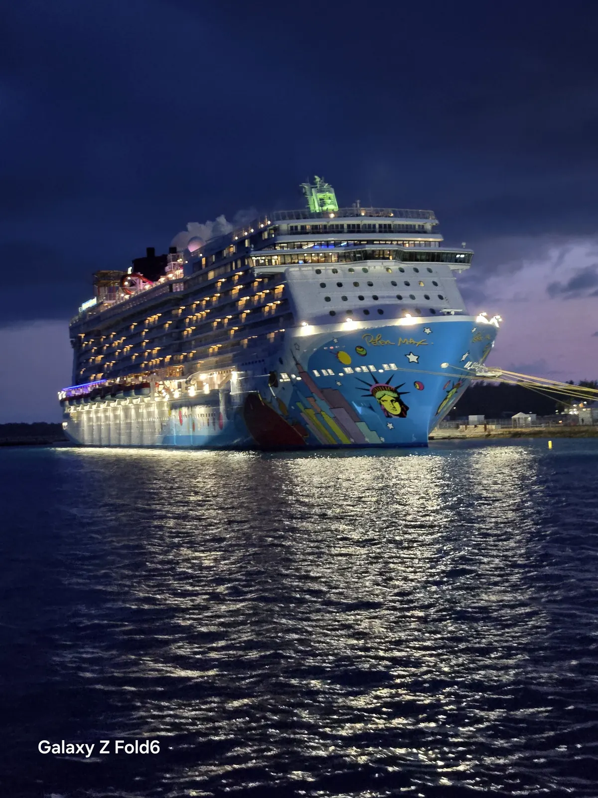 the cruise hq norwegian breakaway lit up at king's wharf bermuda reflected in the water at night