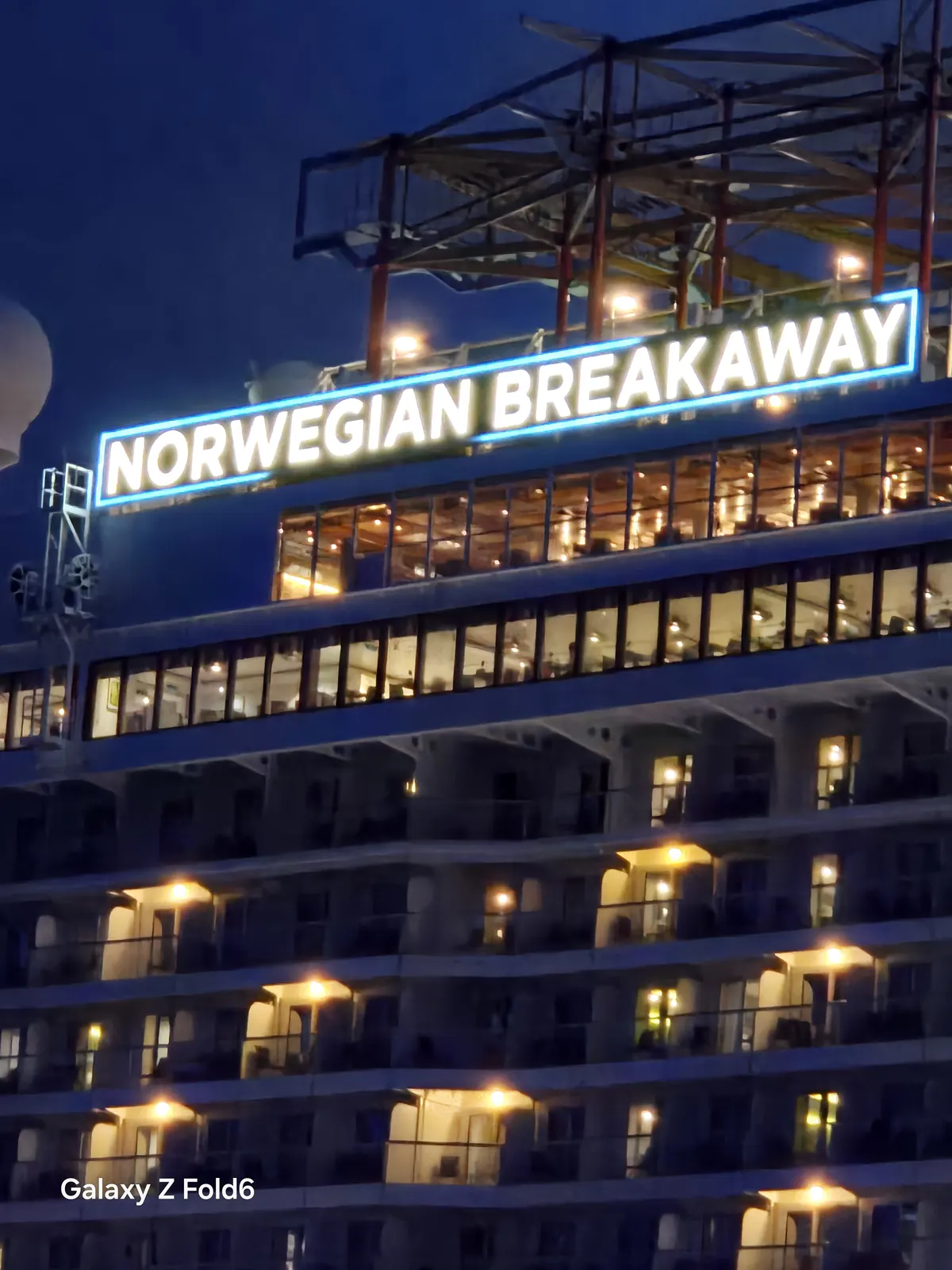 the cruise hq glowing norwegian breakaway name sign above lit cabin decks at night